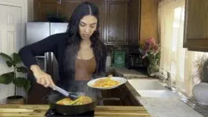 Woman cooking vegetables in a skillet in a cozy kitchen, adding color and flavor to her meal.