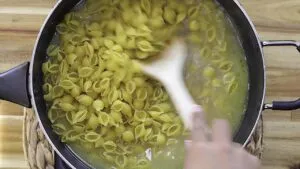 Cooking shell pasta in a pot with a wooden spoon stirring for a delicious meal preparation.