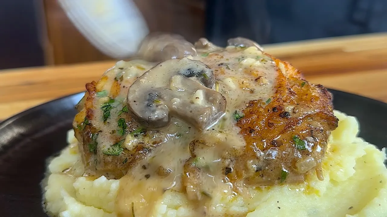 Delicious mushroom gravy sauce chicken over mashed potatoes, garnished with herbs. Perfect comfort food dish.