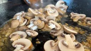 Sliced mushrooms sautéing in a hot skillet with onions, creating a savory dish.
