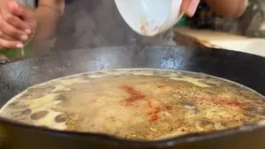 Adding seasonings to a simmering pan for a flavorful dish. Perfect for enhancing savory recipes with aromatic herbs.