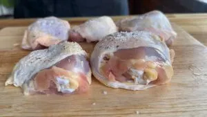 Raw chicken thighs seasoned with salt and pepper on a wooden cutting board.