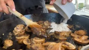 Cooking mushrooms with flour in a skillet, stirring with a wooden spoon.