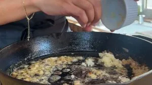 Adding garlic to sauté in a sizzling cast-iron skillet.