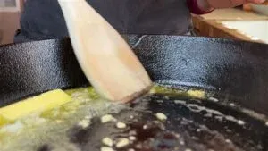 Melting butter in a cast iron skillet with a wooden spatula stirring in garlic.