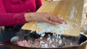 Adding onions to cooking ground beef in a skillet.