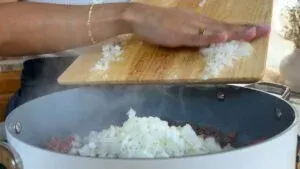 Chopped onions being added to a sizzling pan on the stove for cooking preparation.