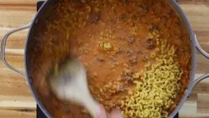 Stirring creamy beef and macaroni pasta in a pot on a wooden surface, creating a hearty meal.