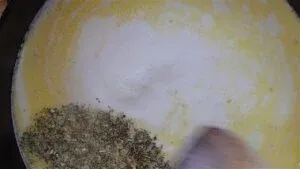 Pot with creamy sauce and herbs being stirred.