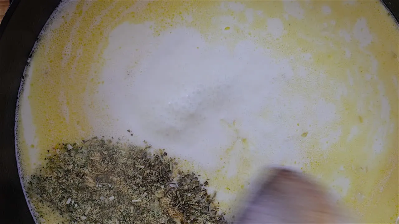 Pot with creamy sauce and herbs being stirred.