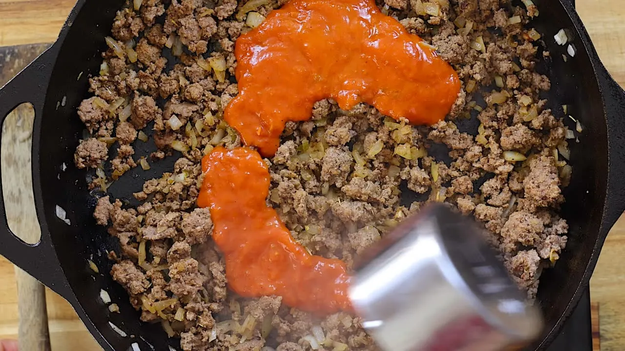 Cooking ground beef with tomato sauce in a skillet for a delicious meal preparation.