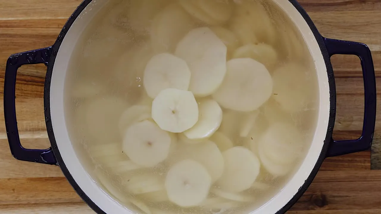 Sliced potatoes soaking in a pot of water on a wooden surface, ready for boiling.