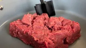 Ground beef being prepared with a meat masher in a gray pan, ready for cooking.