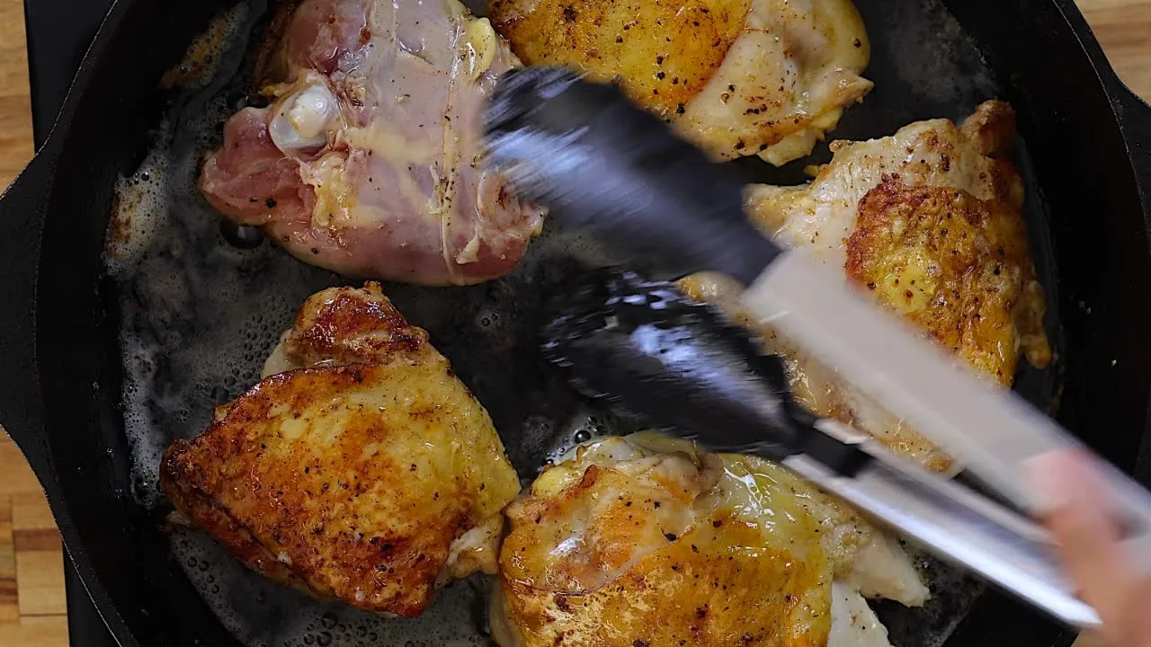 Cooking seasoned chicken thighs in a skillet with tongs.