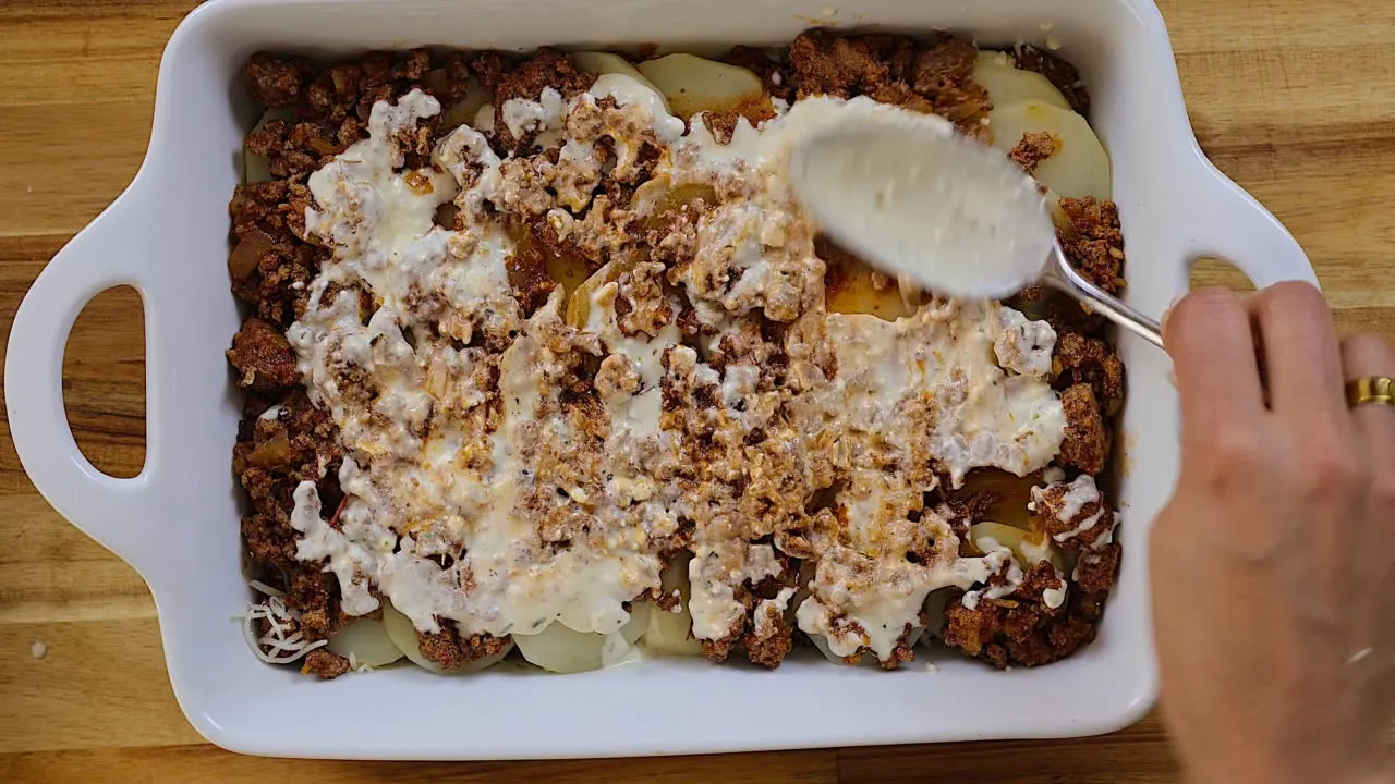 Preparing homemade moussaka: layering minced meat and sauce in a baking dish for a delicious Greek casserole.