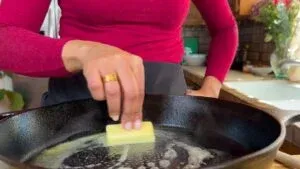 Person melting butter in a hot skillet with a red top, in a cozy kitchen.