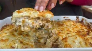 Cheesy potato casserole with creamy sauce being served from a baking dish, topped with golden melted cheese.