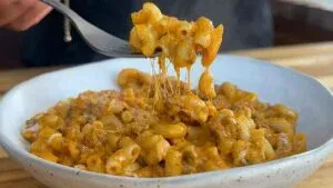 Cheesy macaroni and beef in a bowl, with gooey cheese stretch on fork, perfect comfort food.