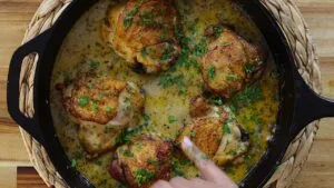Skillet of golden chicken thighs in creamy lemon garlic sauce garnished with parsley.
