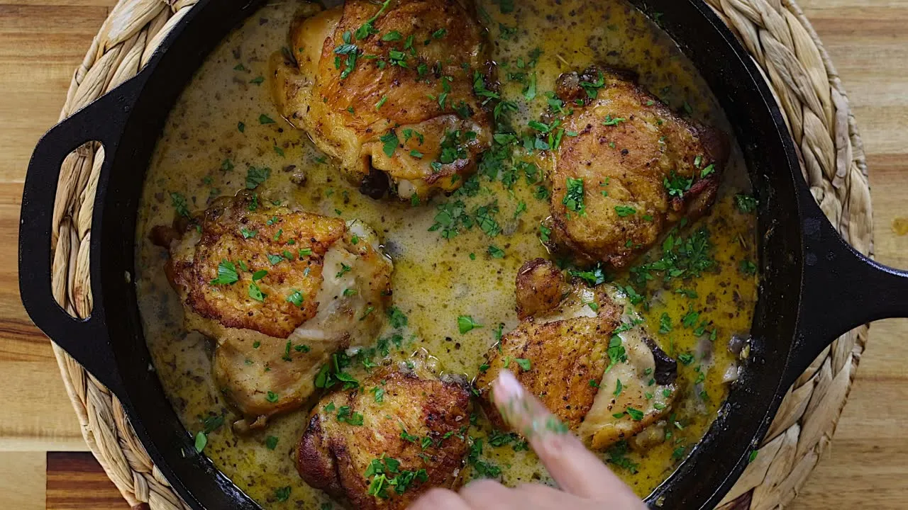 Skillet of golden chicken thighs in creamy lemon garlic sauce garnished with parsley.
