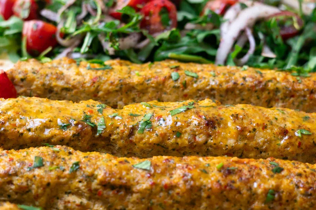 Grilled chicken kebabs with herbs and spices, served with fresh salad in the background.