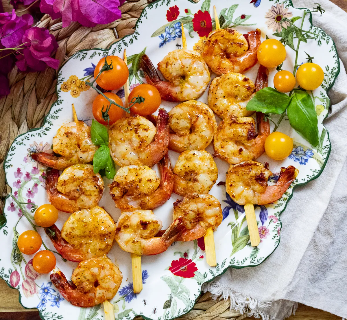 Grilled shrimp skewers with cherry tomatoes and basil on a floral plate.