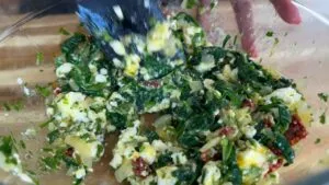 Mixing spinach with feta and sundried tomatoes in a glass bowl for a delicious Mediterranean dish.