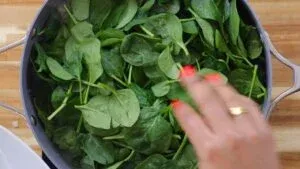 Fresh spinach leaves being stirred in a pan on a wooden table.