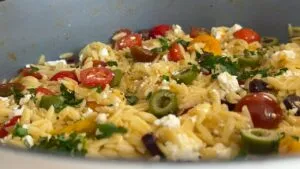 Delicious orzo salad with cherry tomatoes, olives, feta cheese, and fresh basil in a bowl.