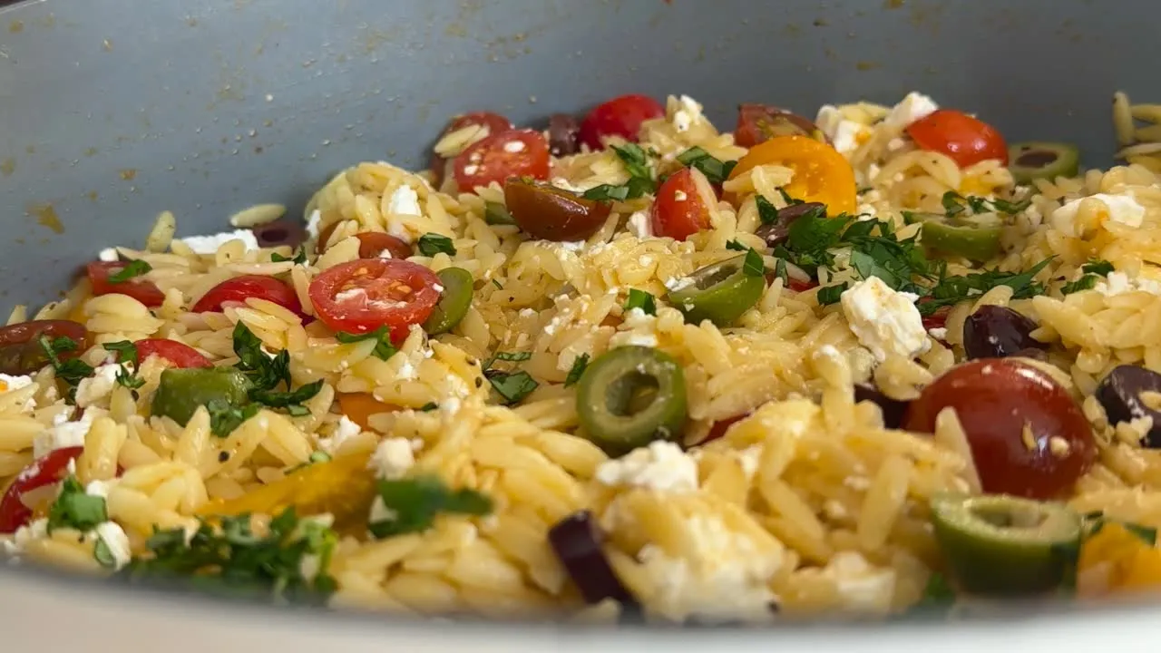 Delicious orzo salad with cherry tomatoes, olives, feta cheese, and fresh basil in a bowl.