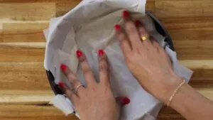 Hands lining a baking pan with phyllo dough on a wooden surface, preparing for baking.