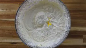 Creamy batter with yellow coloring in a glass bowl on a wooden table. Perfect for baking enthusiasts.