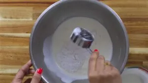 Mixing flour and cream in a steel bowl with a measuring cup on a wooden surface.