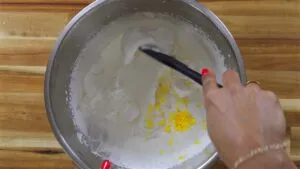 Mixing lemon zest into whipped cream in a stainless steel bowl on a wooden surface.