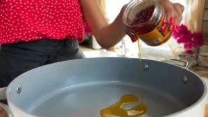 Person pouring oil into a large cooking pan in the kitchen, wearing a red polka dot shirt.