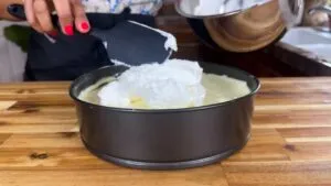 No Bake Cheesecake: Adding whipped cream to a springform pan on a wooden countertop.