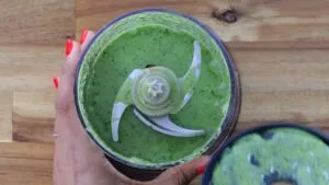 Blending vibrant pesto sauce in food processor on wooden table, close-up of refreshing homemade recipe.