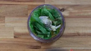 Fresh basil, garlic, and seasonings in a blender ready to make homemade basil sauce on a wooden table.