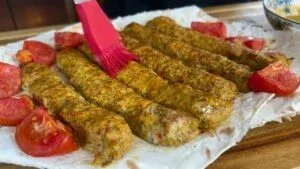 Grilled kebabs brushed with sauce on flatbread, garnished with sliced tomatoes.