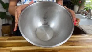 Person holding an empty chilled stainless steel mixing bowl in a kitchen setting.