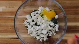 Bowl with egg yolk, feta cheese, and spinach on a wooden table, ready for mixing in a recipe.