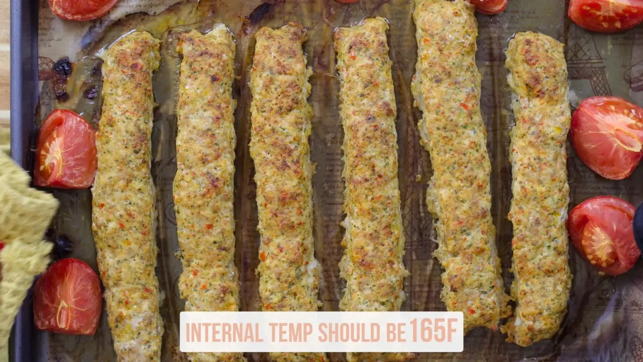 Baked chicken kebabs on a tray with tomatoes; internal temp should be 165F. Perfect for grilling or baking recipes.