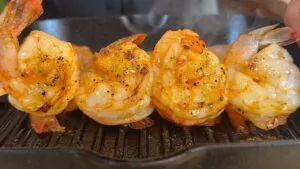 Grilled shrimp sizzling on a hot grill pan, seasoned with herbs and spices.