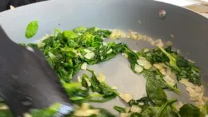 Sautéing fresh spinach and onions in a pan for a healthy and delicious meal.