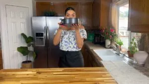 Woman holding a cake pan in a cozy kitchen with wooden cabinets and fresh flowers.