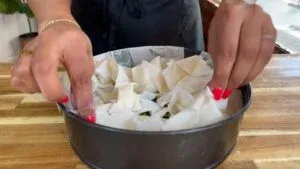 Person assembling phyllo dough in a round baking pan on a wooden surface for a savory pie.