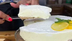 Slice of creamy lemon cheesecake being served with lemon garnish and mint leaves.