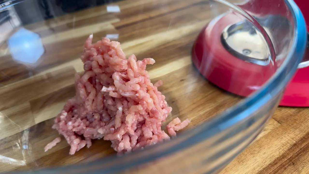 Ground meat in a glass bowl on a wooden counter beside a red kitchen appliance.