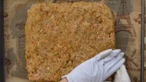 Gloved hand shaping seasoned minced chicken mixture on parchment paper.
