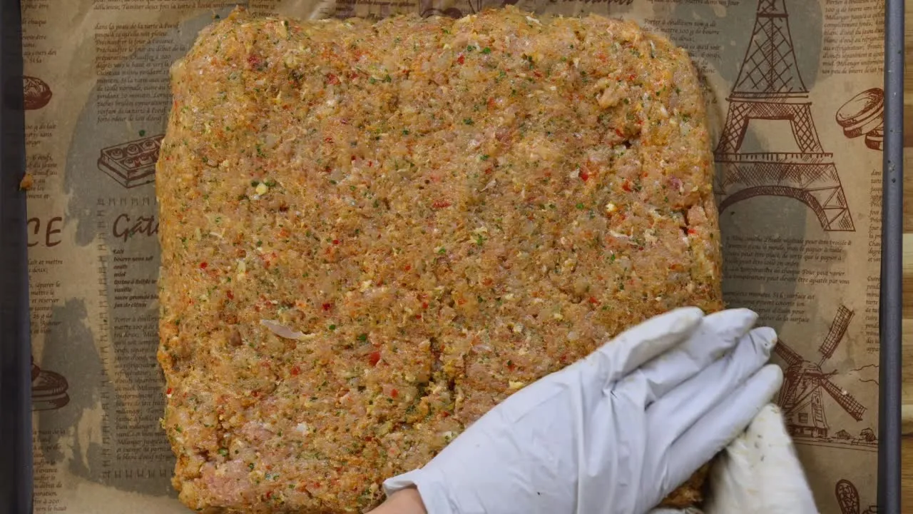 Gloved hand shaping seasoned minced chicken mixture on parchment paper.
